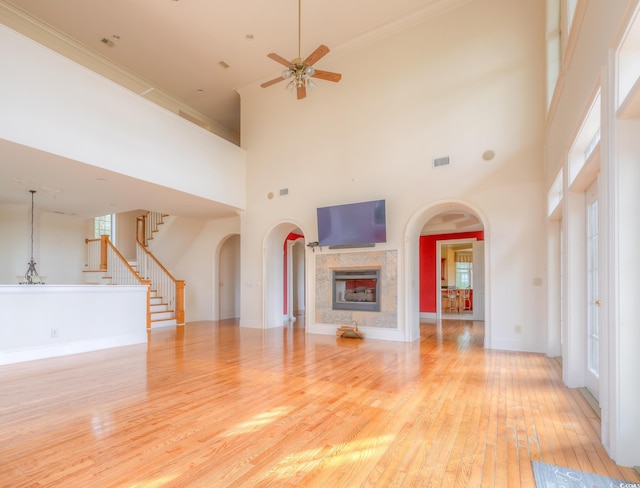 unfurnished living room with ceiling fan, light wood-type flooring, a fireplace, and a high ceiling