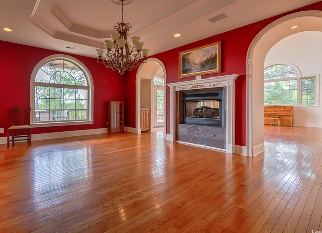 unfurnished living room featuring a multi sided fireplace, an inviting chandelier, light hardwood / wood-style floors, and a tray ceiling