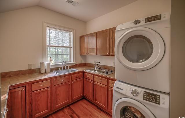 laundry room featuring cabinets, stacked washer and clothes dryer, sink, and light wood-type flooring