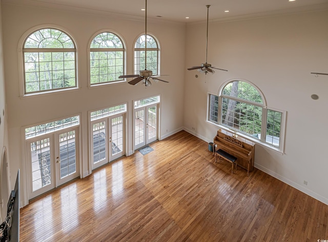 foyer entrance featuring light hardwood / wood-style floors, ceiling fan, french doors, a towering ceiling, and crown molding