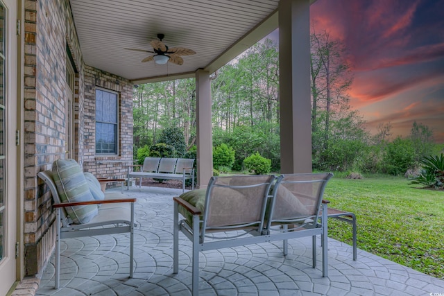 patio terrace at dusk featuring outdoor lounge area, ceiling fan, and a lawn