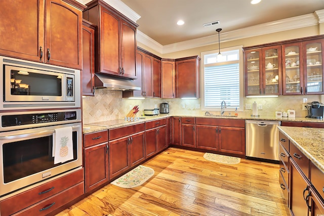 kitchen featuring appliances with stainless steel finishes, light hardwood / wood-style floors, backsplash, hanging light fixtures, and crown molding