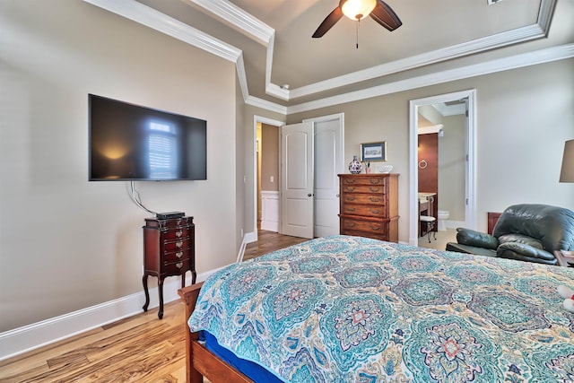 bedroom with ceiling fan, ensuite bathroom, a raised ceiling, crown molding, and wood-type flooring