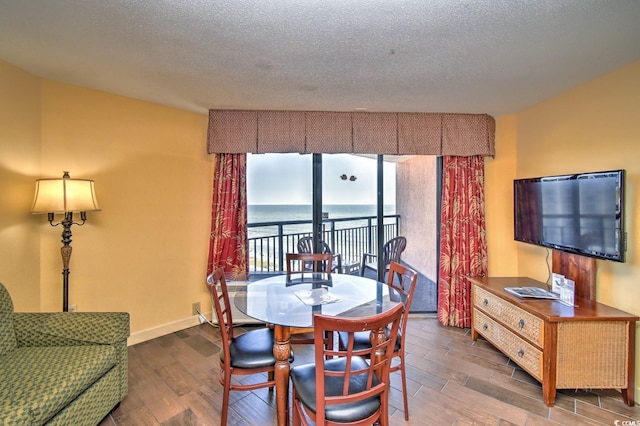 dining area with a water view, a textured ceiling, and dark wood-type flooring