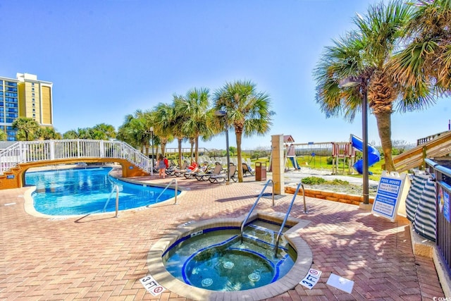 view of swimming pool featuring a community hot tub, a patio area, and a playground