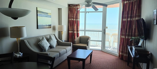 living area with a water view, dark carpet, and ceiling fan