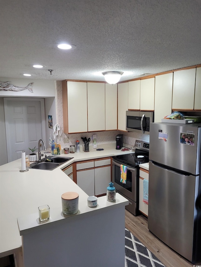 kitchen featuring light wood-type flooring, white cabinetry, stainless steel appliances, sink, and a textured ceiling