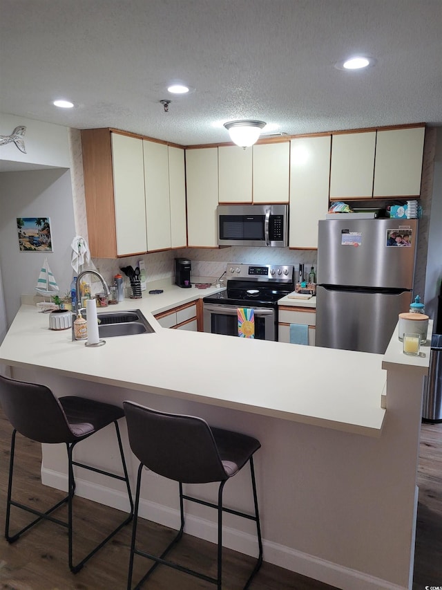 kitchen featuring kitchen peninsula, stainless steel appliances, dark hardwood / wood-style floors, a textured ceiling, and sink