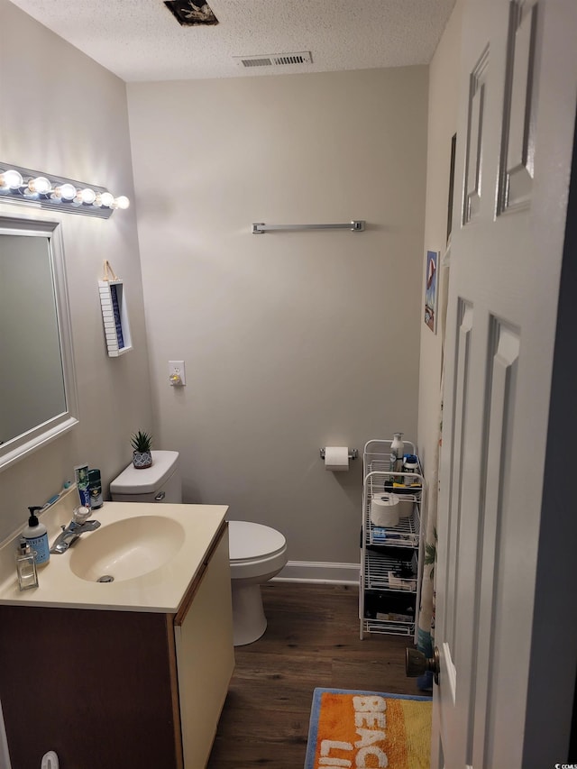 bathroom with a textured ceiling, wood-type flooring, vanity, and toilet