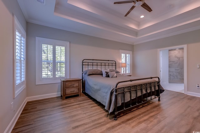 bedroom featuring a raised ceiling, ceiling fan, ensuite bathroom, and hardwood / wood-style flooring