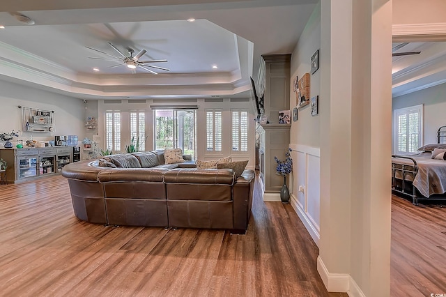 living room featuring ceiling fan, wood-type flooring, a tray ceiling, and crown molding