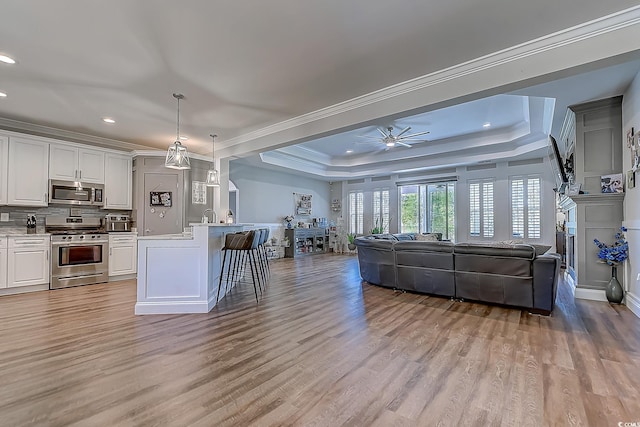 kitchen featuring a raised ceiling, hanging light fixtures, stainless steel appliances, and white cabinetry