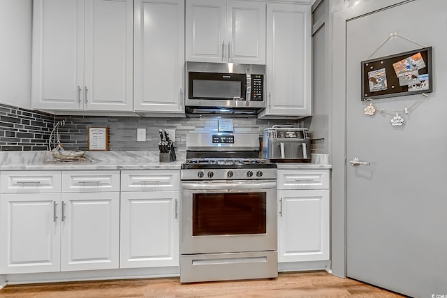 kitchen featuring decorative backsplash, light hardwood / wood-style flooring, stainless steel appliances, white cabinets, and light stone counters