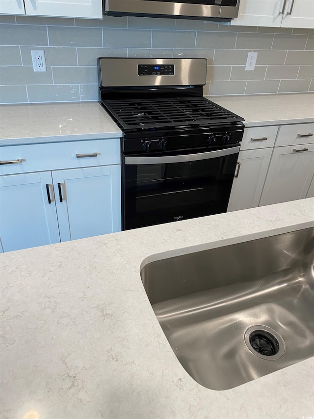 kitchen featuring white cabinetry, stainless steel appliances, light stone counters, and backsplash