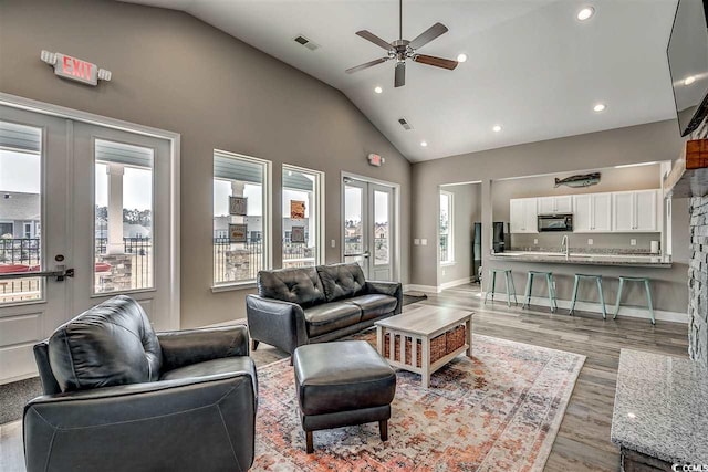 living room featuring light hardwood / wood-style floors, sink, ceiling fan, high vaulted ceiling, and french doors