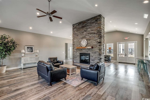 living room with hardwood / wood-style flooring, ceiling fan, a stone fireplace, lofted ceiling, and french doors