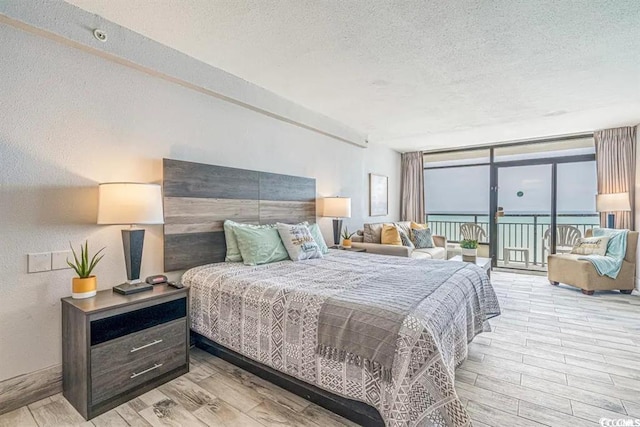 bedroom with a water view, expansive windows, a textured ceiling, access to outside, and light wood-type flooring