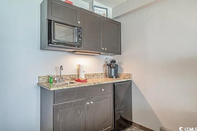 bar with sink, gray cabinets, and light stone countertops