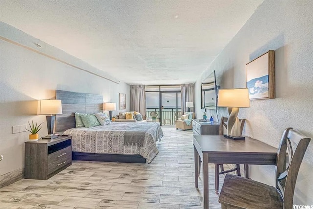 bedroom with a textured ceiling, light wood-type flooring, and a wall of windows