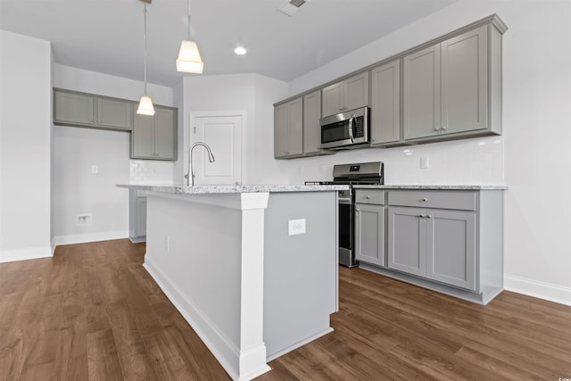 kitchen with gray cabinetry, dark wood-type flooring, a center island with sink, hanging light fixtures, and appliances with stainless steel finishes