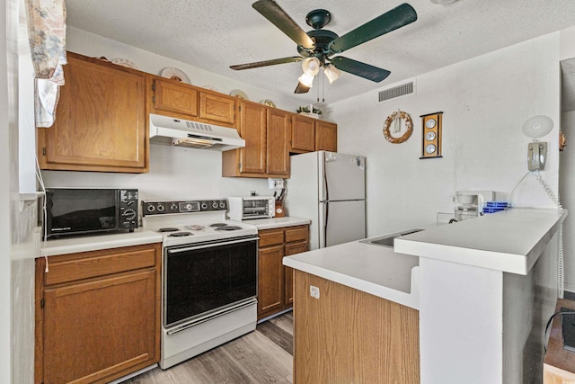 kitchen with white appliances, light wood-type flooring, kitchen peninsula, ceiling fan, and a textured ceiling