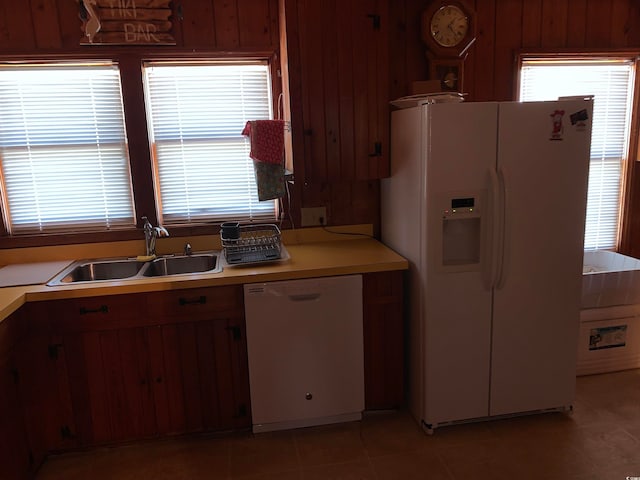 kitchen with light tile floors, wood walls, white appliances, and sink