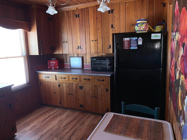 kitchen featuring hardwood / wood-style flooring, wood walls, and black fridge