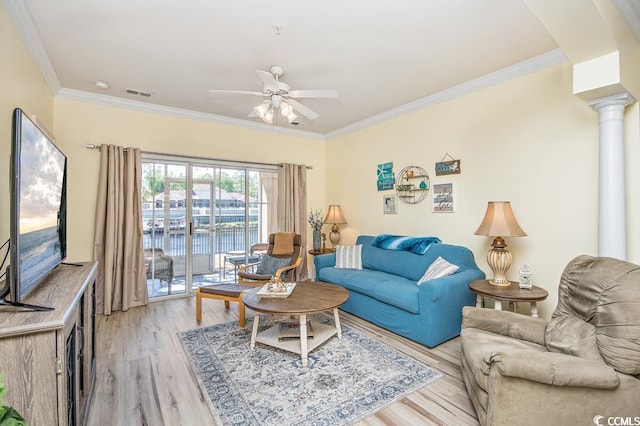 living room with ceiling fan, a water view, light wood-type flooring, decorative columns, and ornamental molding