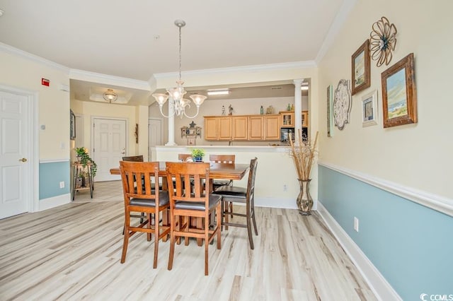 dining area with ornamental molding, decorative columns, light wood-type flooring, and an inviting chandelier