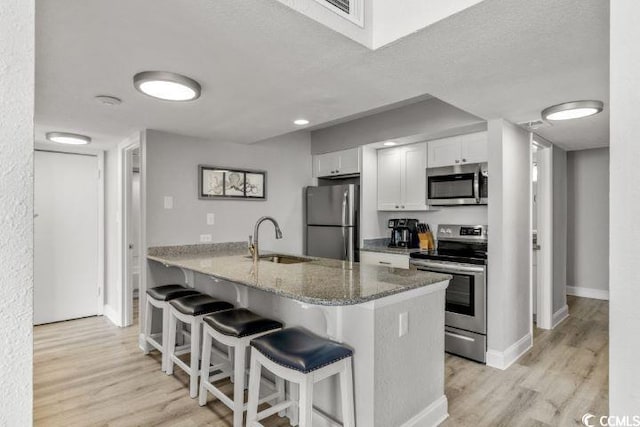 kitchen featuring light stone countertops, white cabinetry, appliances with stainless steel finishes, sink, and light hardwood / wood-style floors