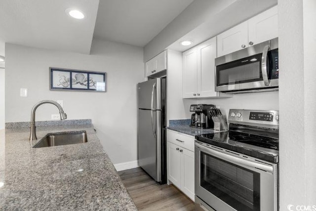 kitchen with white cabinets, hardwood / wood-style floors, stainless steel appliances, sink, and dark stone countertops