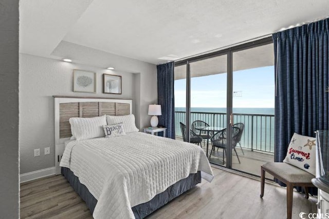 bedroom with a water view, expansive windows, hardwood / wood-style floors, and access to outside