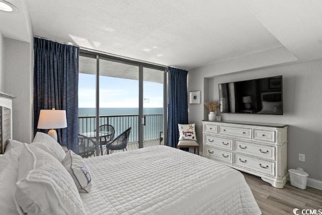 bedroom featuring hardwood / wood-style floors, a wall of windows, a water view, and access to outside