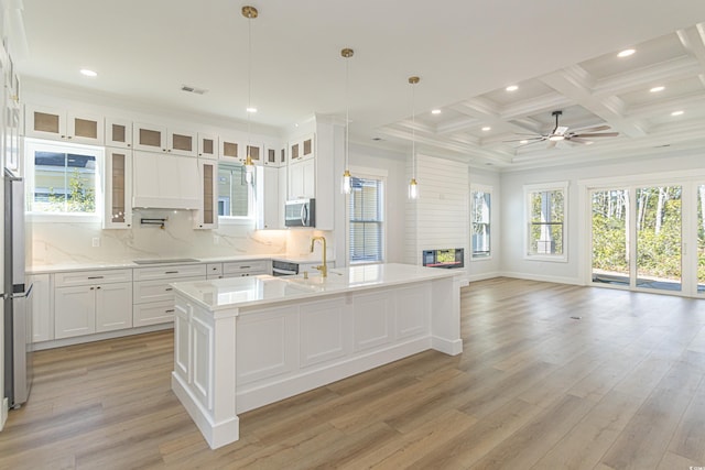 kitchen with a center island with sink, stainless steel microwave, glass insert cabinets, open floor plan, and white cabinets