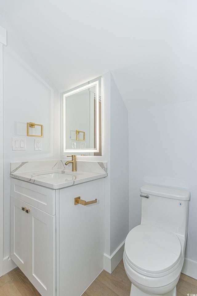 bathroom with baseboards, lofted ceiling, toilet, wood finished floors, and vanity