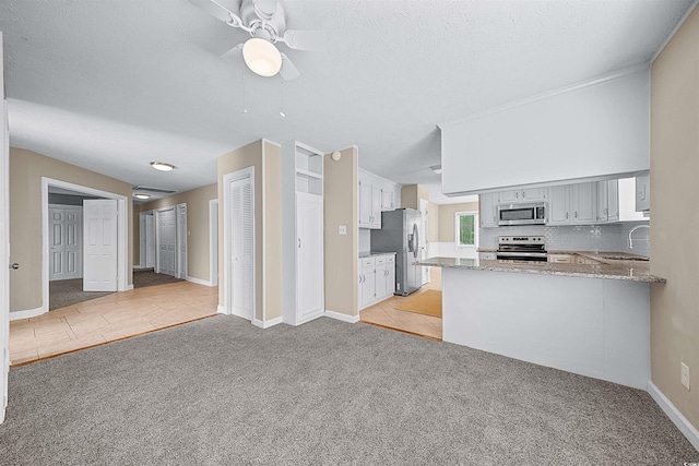 kitchen featuring light colored carpet, appliances with stainless steel finishes, kitchen peninsula, and ceiling fan