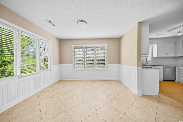 interior space with light stone countertops, a textured ceiling, tasteful backsplash, light tile floors, and stainless steel dishwasher