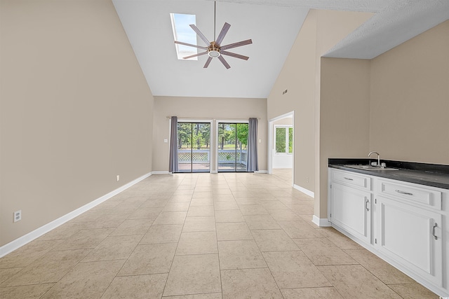 unfurnished living room featuring high vaulted ceiling, light tile floors, sink, a skylight, and ceiling fan