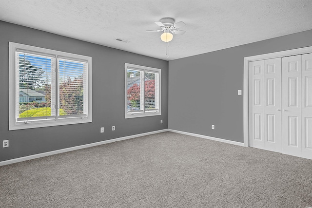 spare room featuring a healthy amount of sunlight, carpet flooring, ceiling fan, and a textured ceiling