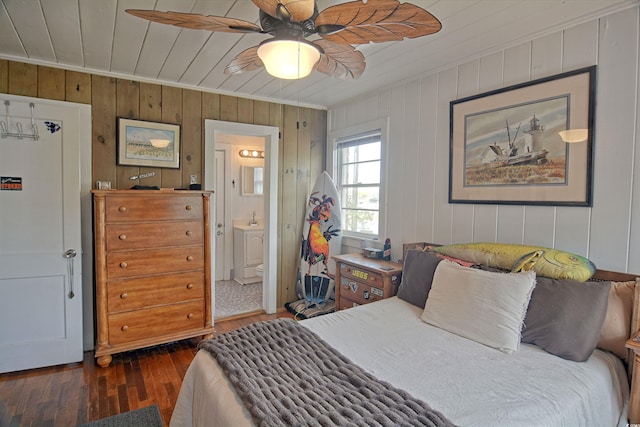 bedroom featuring ceiling fan, wooden walls, ensuite bathroom, and dark wood-type flooring