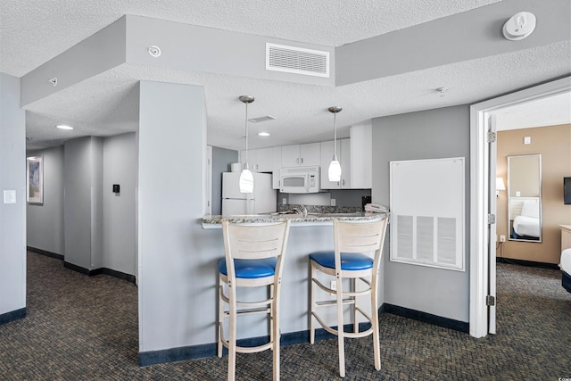 kitchen featuring dark colored carpet, kitchen peninsula, white appliances, a textured ceiling, and white cabinetry