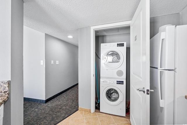 laundry room featuring a textured ceiling, light tile flooring, and stacked washing maching and dryer