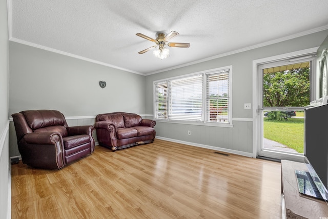 living area with a textured ceiling, ceiling fan, light wood-type flooring, and ornamental molding