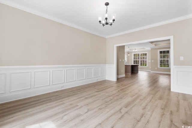 spare room with an inviting chandelier, crown molding, and light wood-type flooring