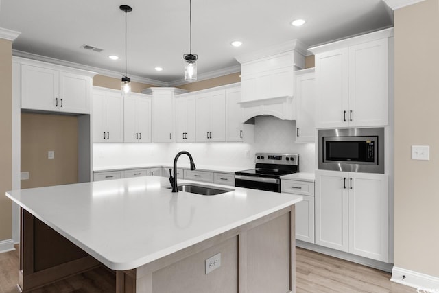 kitchen with appliances with stainless steel finishes, sink, light hardwood / wood-style floors, decorative light fixtures, and a center island with sink