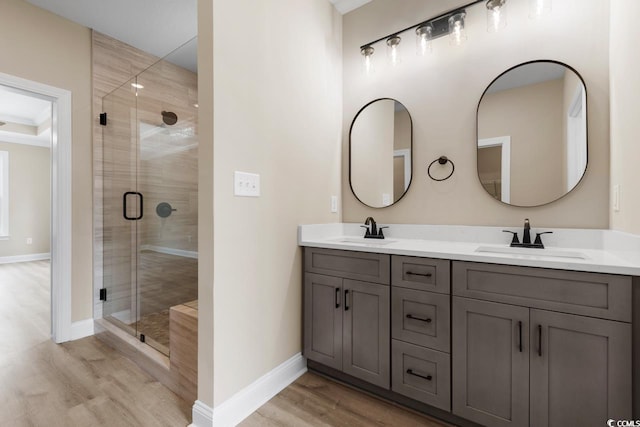 bathroom with wood-type flooring, a shower with shower door, vanity with extensive cabinet space, and dual sinks