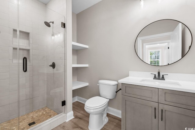 bathroom featuring wood-type flooring, a shower with shower door, vanity with extensive cabinet space, and toilet