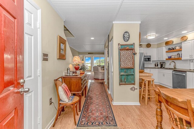 interior space featuring dishwasher, white cabinets, sink, light wood-type flooring, and a breakfast bar