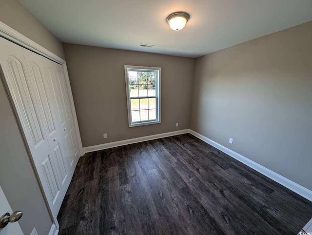 unfurnished bedroom with a closet, visible vents, dark wood-type flooring, and baseboards