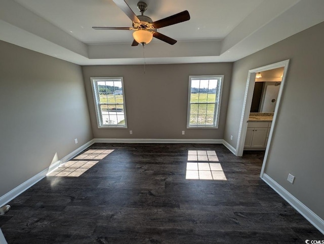 unfurnished bedroom featuring a raised ceiling, multiple windows, and dark wood-style floors